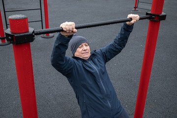 Adult man performing pull-up exercise at an outdoor gym, holding onto bar. Strength training in public fitness area. Outdoors