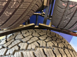 New Tires on Rack: Close-up detail of black rubber tire treads stacked on a storage rack in a shop.