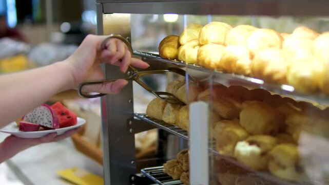 Customer selects freshly baked multigrain bread using gloves in a bakery. Variety of artisan loaves displayed behind glass in a self-service section of a modern grocery store. Daily fresh crusty bread