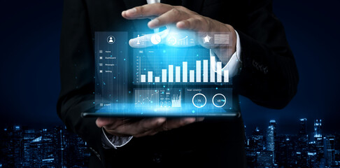 A business professional presents a modern digital dashboard with financial data and graphs on a laptop screen, set against an urban night skyline. Impute
