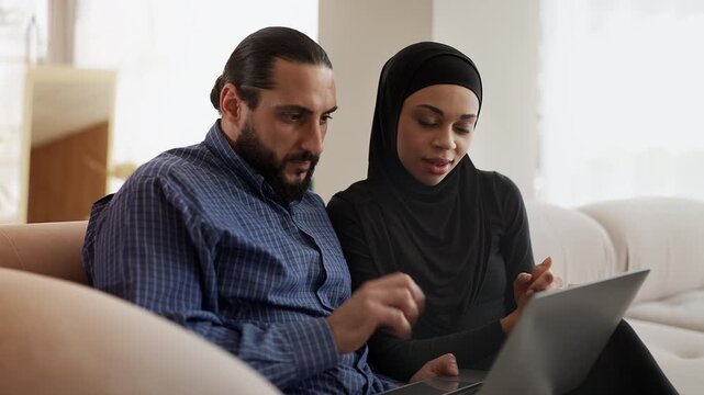 Cheerful Muslim couple selecting new apartments on laptop, online shopping