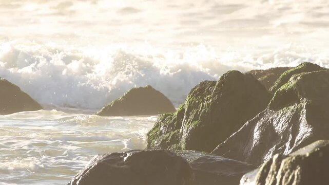 Foamy ocean waves illuminated by strong sunlight as they break against coastal rocks, creating a glowing seascape.