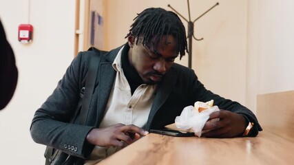 Focus on phone as dark skinned man gives mouth widening expression while eating indoors, appearing to dislodge food gently, lighting and wooden surface adding warmth to everyday realistic atmosphere