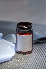 Empty brown glass jar with blank label on gray textured surface with papers and cloth nearby.