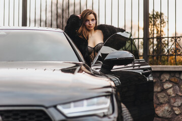 Photo, portrait of a beautiful young sexy woman, a model girl in a fur coat with a chic expensive black car on a city street outdoors.