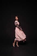 young woman is dancing in a national dress on black background