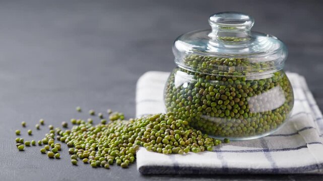 mung beans in glass storage jar on a black marble background.  green mung beans in a storage glass jar on a dark kitchen table.
