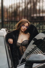 Photo, portrait of a beautiful young sexy woman with glasses, a model girl in lingerie, in a fur coat with a chic expensive black car on a city street outdoors.