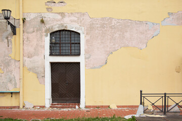 A yellow wall of an old building with a brown door and crumbling plaster