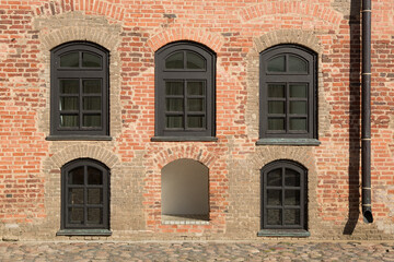 An old brick wall with five arched windows in a brown frame
