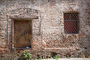 Brick wall of an old house, a window with bars and a rusty door.