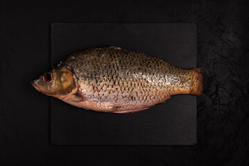 whole gutted carp on black background. Fresh raw freshwater fish lies on a stone cutting board....