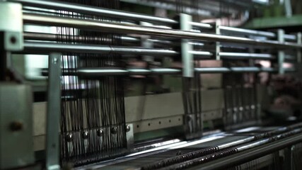 Closeup shows an industrial weaving machine running at high speed as black warp threads move rapidly through metal guides forming textile structure
