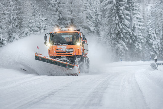 Snow plow clear and sprinkles snowy road in a snowstorm.