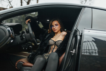 Naklejka premium A photograph, a portrait of a beautiful young woman, a female model in a fur coat, in women's lingerie, sitting, posing inside an expensive luxury premium car.