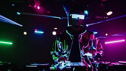 DJ performs live set in nightclub. Colorful lights create vibrant atmosphere. Young crowd enjoys electronic music experience. Energy fills dance floor.