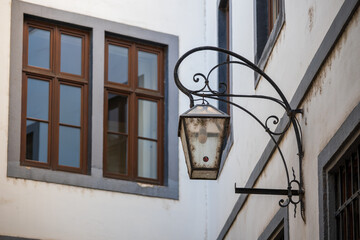 Old wall-mounted street lantern attached to a historic building facade with wooden windows and decorative metal bracket.