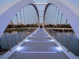 Obraz premium Modern White Pedestrian Bridge with Blue Led Lighting Over Water at Dusk