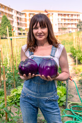 Woman proudly holding large round eggplants harvested from a community or personal garden