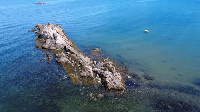 Close-up flyover of a rocky reef showing its texture eroded by weathering and tides in a tranquil bay where a rowboat is moored and seabirds are resting. Anse du Petit Mitis, St. Lawrence River.