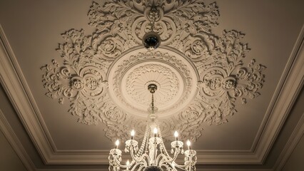Low angle view of an ornate classical plaster ceiling rose with intricate floral moldings and a hanging crystal chandelier