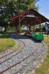 Miniaturowa stacja kolejowa z kolorowymi wagonikami pod drewnianą wiatą w parku - Cichowo. © Pol Badger