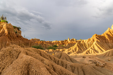 Golden sunlight crowns cracked Tatacoa Desert ridges under gray skies