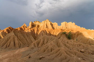 Naklejka premium Sunlit peaks of Tatacoa Desert mounds under brooding gray clouds