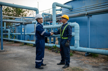Two industrial engineers stand shaking hands at a water plant site.