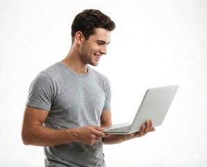 Smiling young man holding and looking at a laptop with a happy expression while standing isolated.