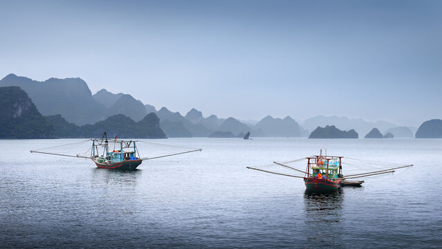 Evening is approaching, and squid fishing boats are gently swaying on the mild waves of Ha Long Bay, Vietnam, Asia. - Powered by Adobe