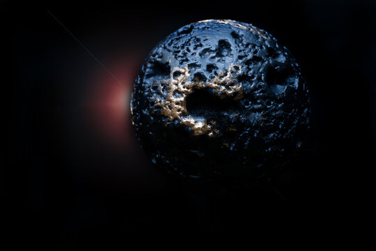 Macro photo of a porous plastic sphere. Mysterious dark planet or asteroid in deep space. Sci-fi concept of dangerous meteorite flight with crater texture and lens flare effect. Photo