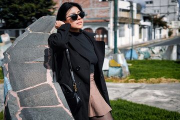 Obraz premium Woman posing outdoors wearing black coat and sunglasses