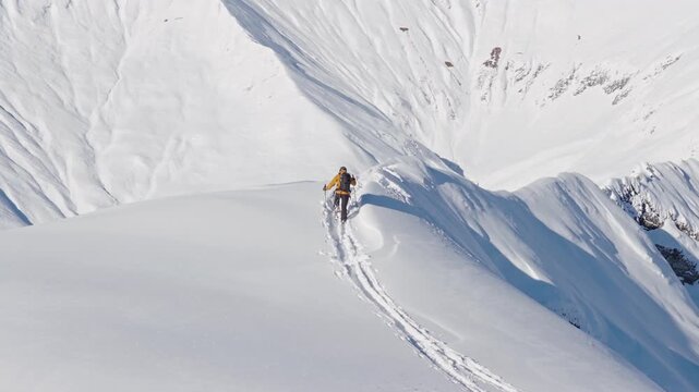 Aerial footage of a ski mountaineer ascending a snowy alpine ridge in Austria. Winter landscape, backcountry adventure, and solitude in breathtaking mountain scenery captured in 4K.