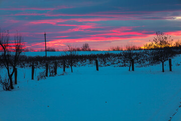 A fantastic celestial dawn or dusk paints the horizon and clouds in rich shades of fuchsia and pink, creating a dramatic contrast with the cold, blue snow field.
