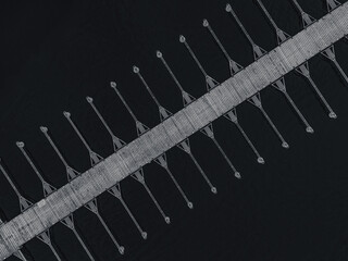 Aerial view shows a long, empty pier extending into still waters. The structure features evenly spaced supports, creating a pattern against the serene backdrop