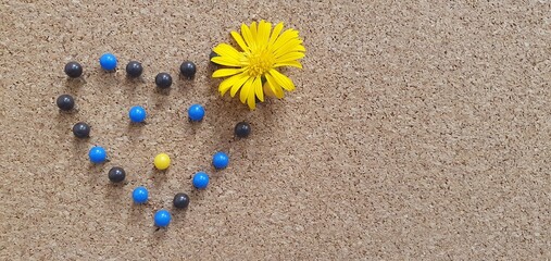 A heart shape created from blue, black, and yellow push pins on a cork board, decorated with a bright yellow flower. Ideal for themes of love, creativity, positivity, inspiration and romance design.