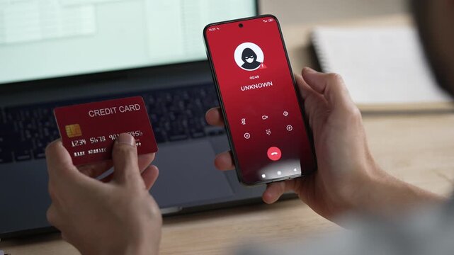 A credit card user giving the credit card number to a scammer while holding a phone showing a scammer on the line