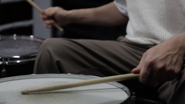 Drummer hands striking snare drum with sticks, captured midperformance showing motion blur, textured drumhead, casual stage clothing and focused groove driving live club energy