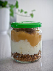 Layering healthy breakfast or snack in a glass jar with fruit puree, yogurt, and granola on a modern kitchen counter, suggesting fresh and nutritious eating