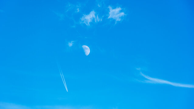 Luna creciente foto diurna al atardecer con nubes blancas y estela de avi&oacute;n