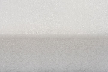 A horizontal close-up shot showing the edge of a bright white, fine-pored plastic foam or sponge material
