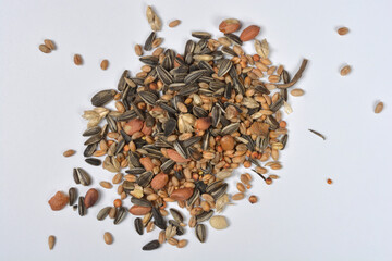 An isolated, overhead shot of a small mound of mixed bird seeds, including sunflower seeds and peanuts, scattered on a white background