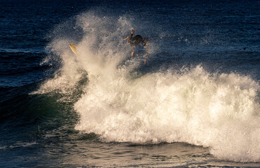 A surfer wearing a wetsuit wiping out on the lip of a wave