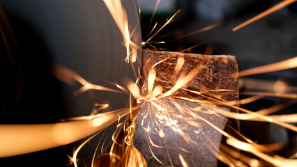 Metal grinding machine shaping a rusty iron piece, creating a bright shower of sparks flying in a dark industrial environment, representing hard work and manufacturing processes
