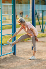 Obraz premium Active Senior Woman Doing Leg and Hip Stretching on Outdoor Equipment.