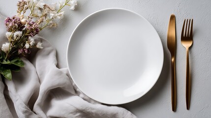 Stylish empty plate setting with gold cutlery and delicate floral arrangement for elegant dining and upscale restaurant promotions on a light grey surface