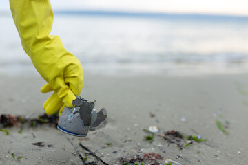 volunteer picking up a crushed metal can during beach cleanup, highlighting pollution, waste...