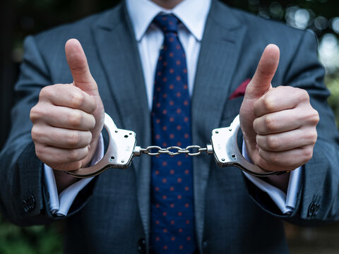 Successful businessman giving thumbs up with handcuffs symbolizes overcoming challenges and achieving financial freedom, representing resilience and determination