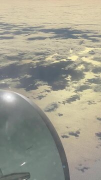 Vertical video. View from an airplane window of a layer of clouds casting shadows on the surface of the Mediterranean Sea.